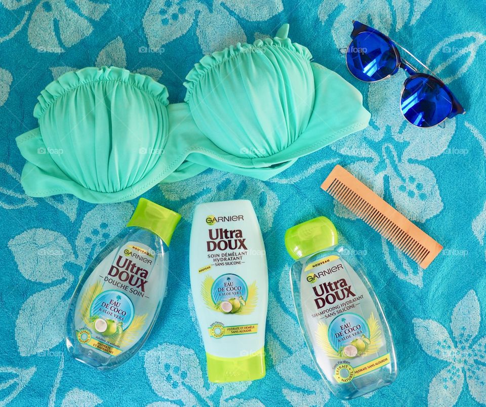 Garnier eau de coco shampoo, conditioner and bath gel on a blue towel with comb and sunglasses and bikini top.