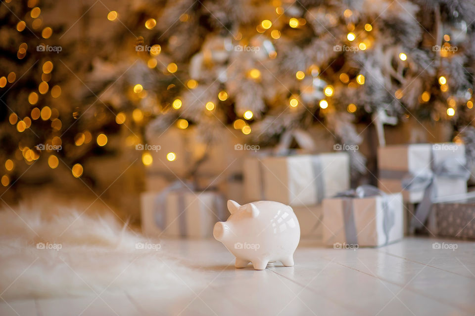 piggy bank with 100 dollars banknote in festive New Year atmosphere of scenery.  Magical bokeh with Christmas tree and bright lights.