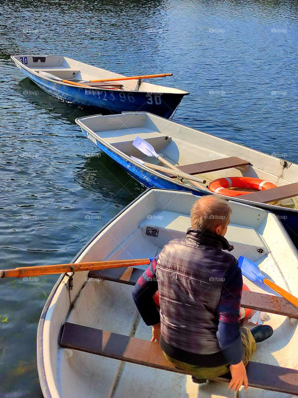 The blue water of the river, along which three boats float, tied to each other.  There is a man in the first boat.  Two boats are empty