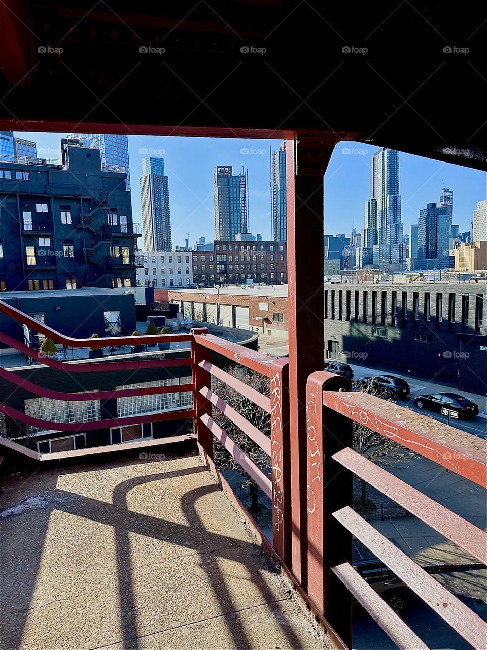 This is the red metal staircase on the “Greenpoint”, Bklyn side of the “Pulaski Bridge” looking out onto “THE BOX HOUSE HOTEL” which is the large black building on the left on a sunny afternoon in late December 2023. Hypnotic Productions