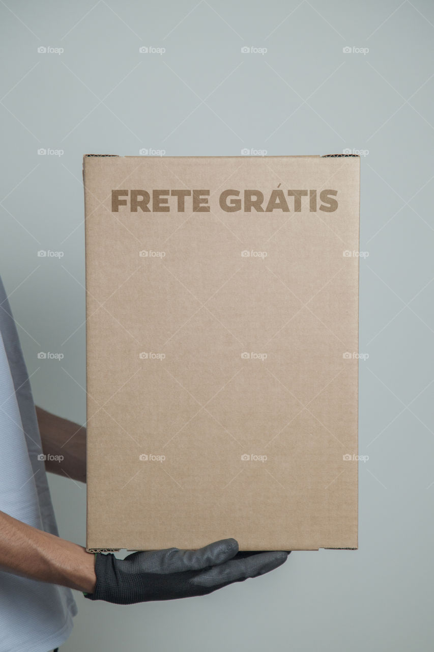 Detail of man with black gloves holding a cardboard box written free shipping to deliver products on gray background. Delivery concept. Delivery service concept. Copy space. Black friday concept.