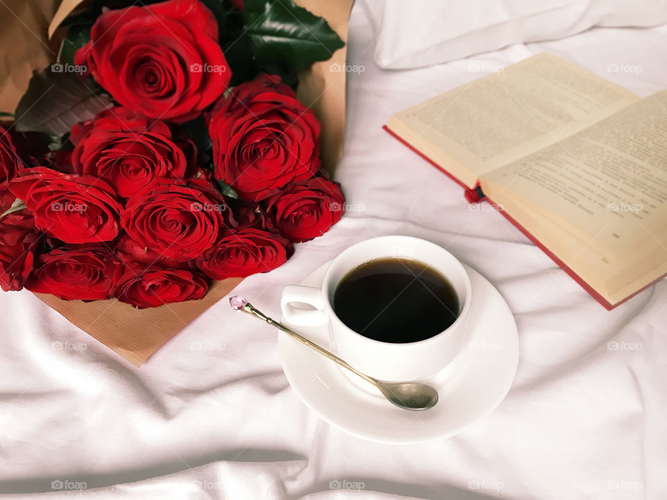 Coffee cup in white bed with red roses and red book 