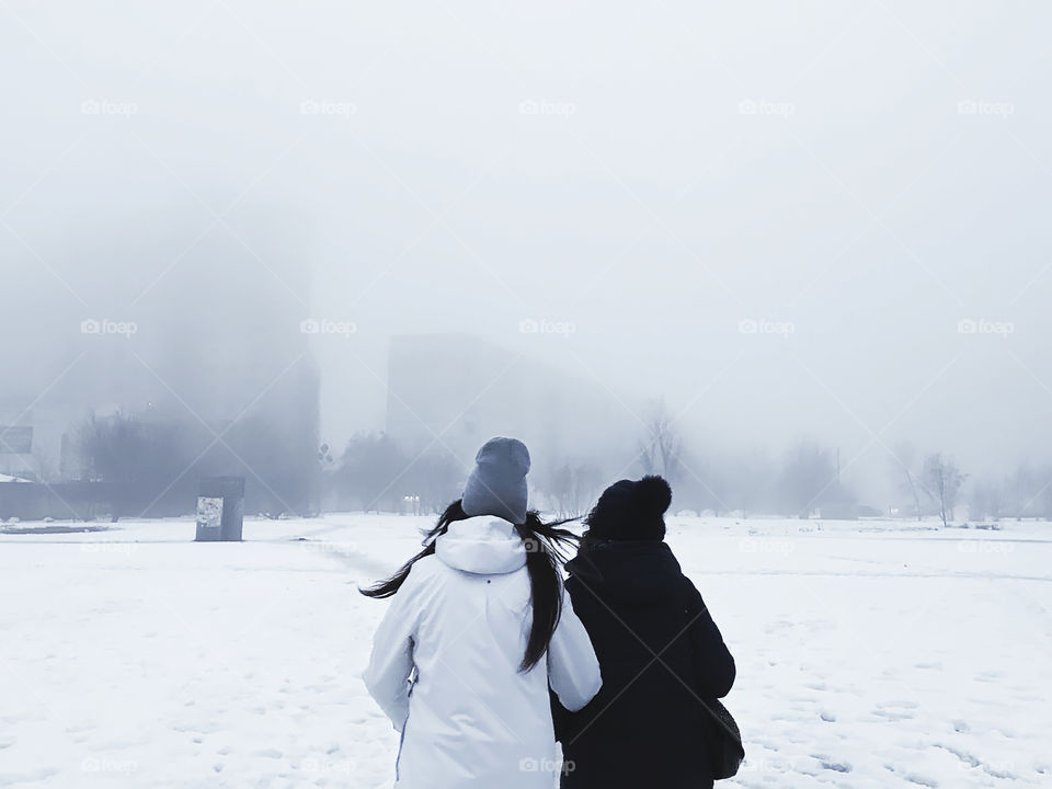 Two women walking by the misty city in winter 