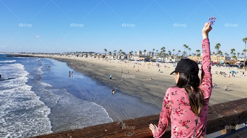 fashionable woman looking out the sea view of the ocean holding up a flower