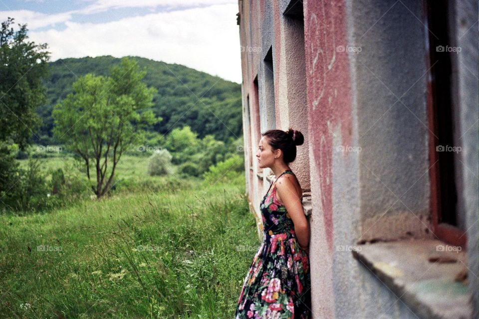 Woman dressed in a beautiful dress standing near a abandoned building; taken with an olympus om101.