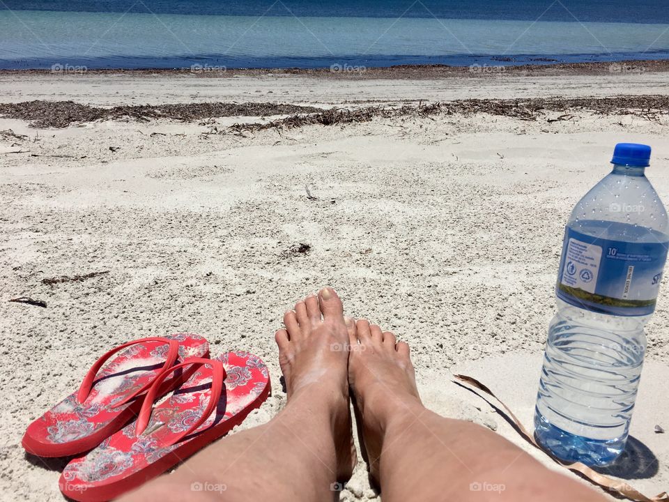 Bare legged and barefoot woman wearing denim skirt laying down on beach facing the ocean horizon 