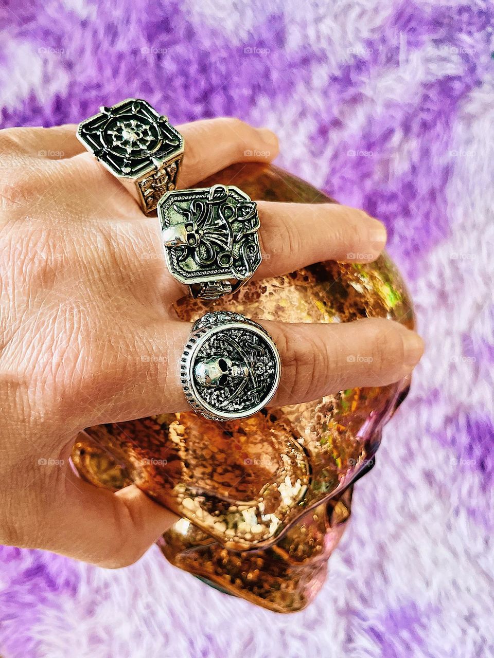 Woman’s hand with lots of rings on holds gold skull, dressing as a pirate, pirate accessories for Halloween costume 