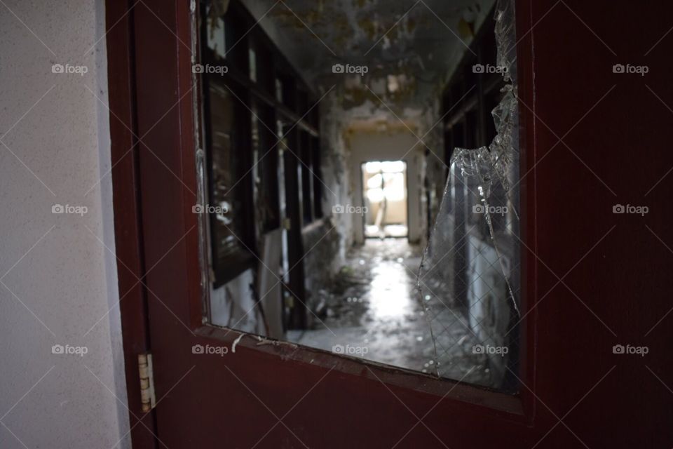 View through a broken door to the hallway of an abandoned prison. 