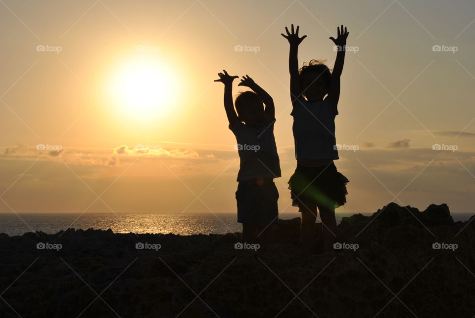 Two children raising their arms  in front of beach