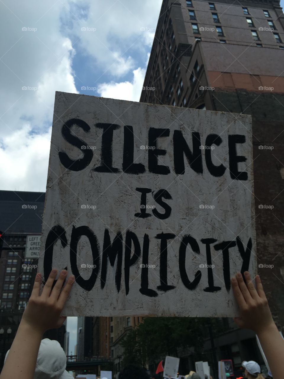 Wooden sign reading “Silence is Complicity”
