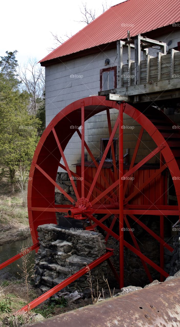 Old mill large red grinding wheel with rock foundation.