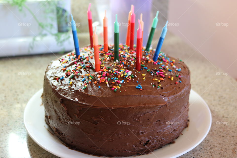 Chocolate birthday cake with sprinkles and candles in a variety of colors. 