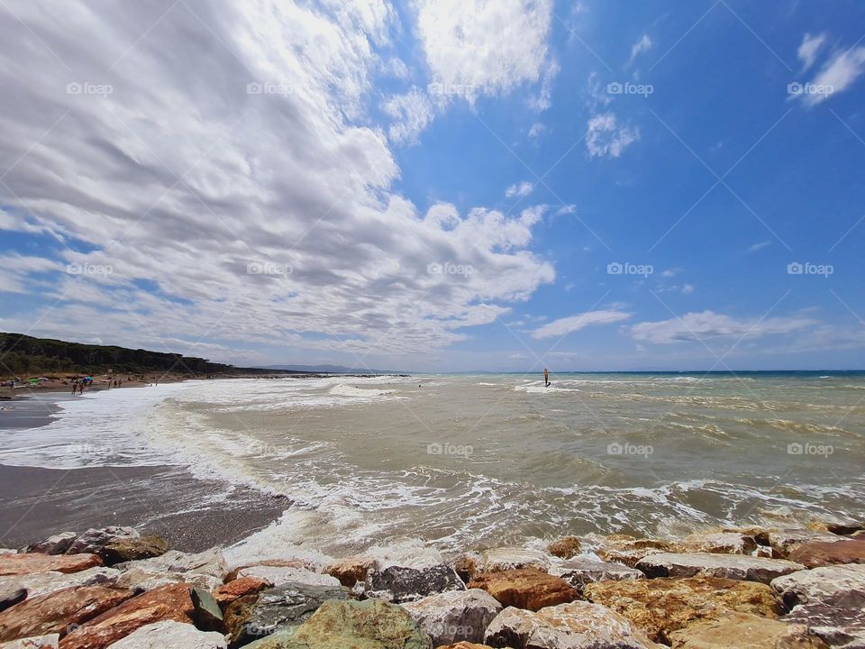 windsurfing between sky clouds and sea