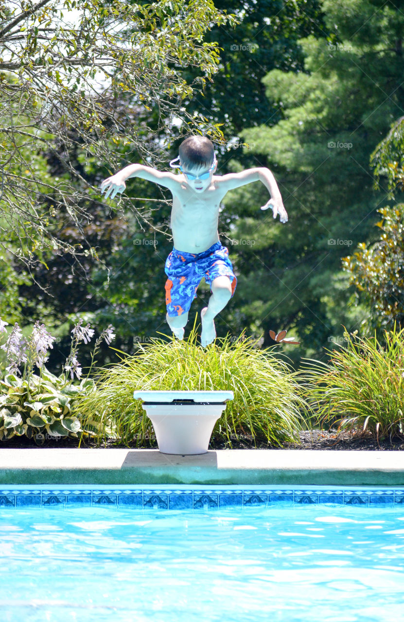 Young boy jumping into a pool off of diving board