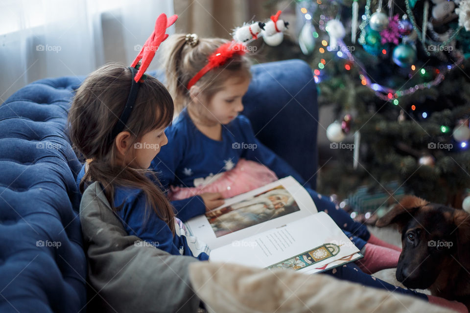 Little sisters reading a book at Christmas time 