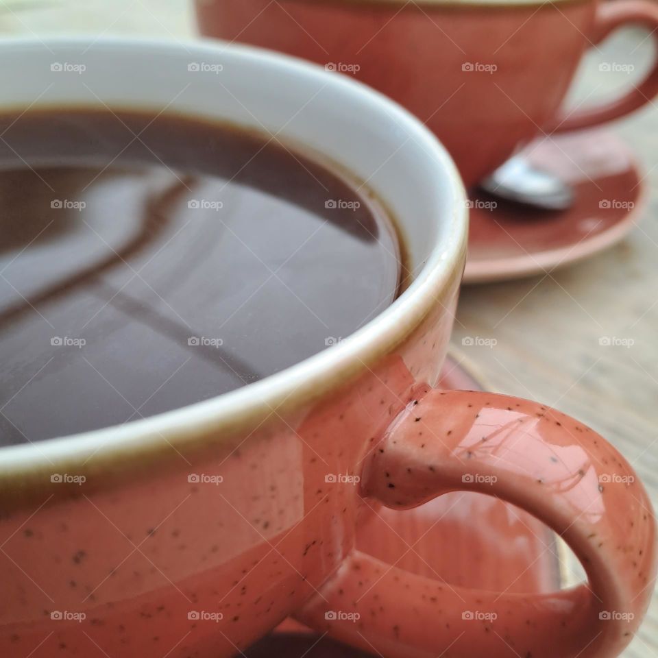 coffee cups orange on saucers. Handles on wooden table. black coffee. reflection in top
