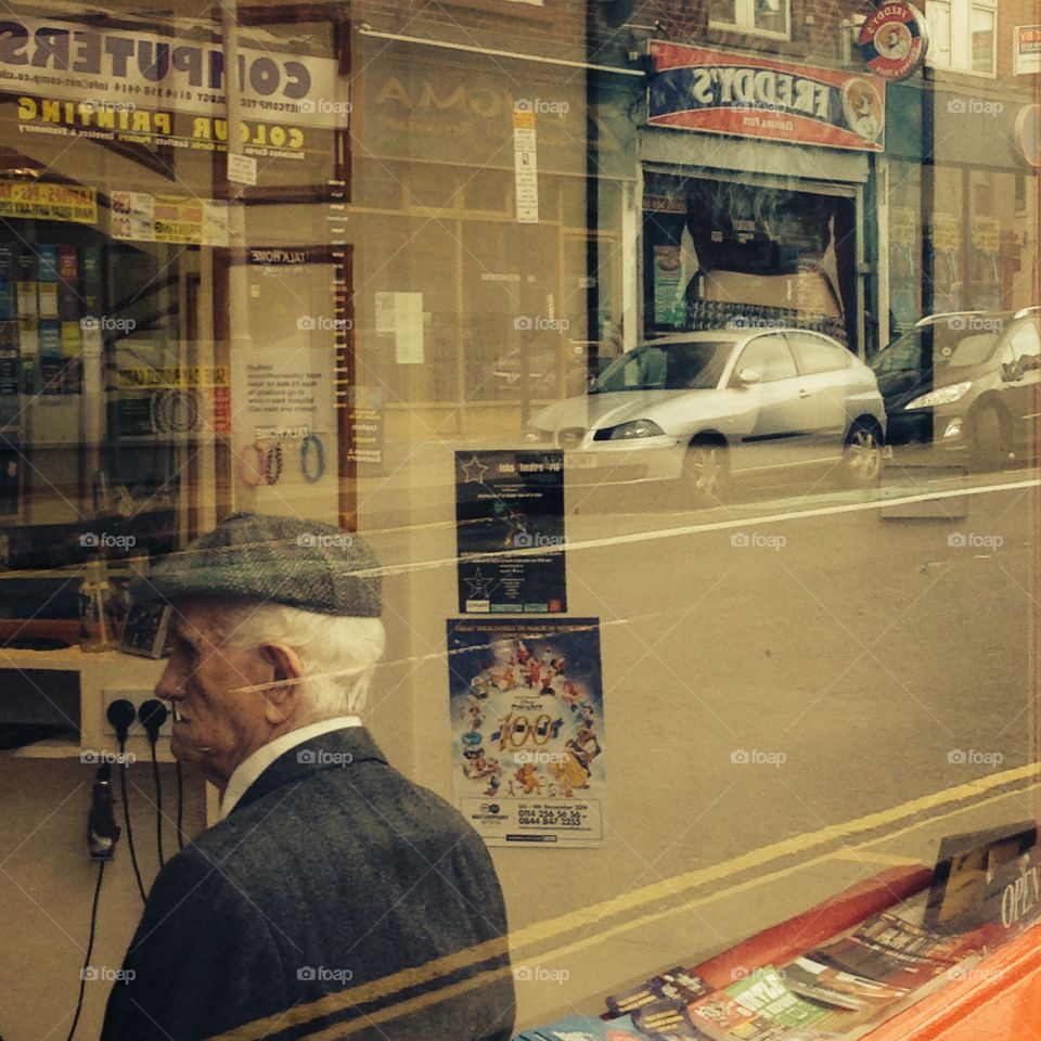 Old man waiting his turn at the barber's, with the street outside reflected in the window