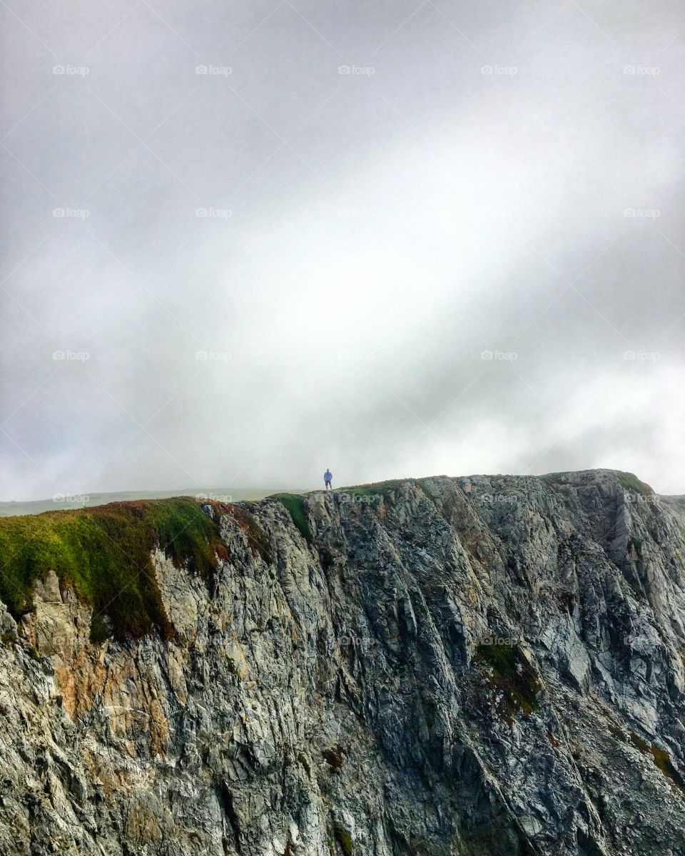 Shot of a man standing alone along the edge of a rocky coast line to show the perspective of his size in comparison to his environment