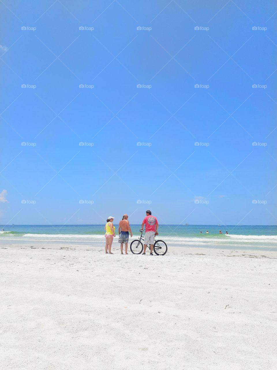 Three friends stand on the beach near the ocean talking at Indian Rocks Beach in Indian Rocks Beach, Florida.