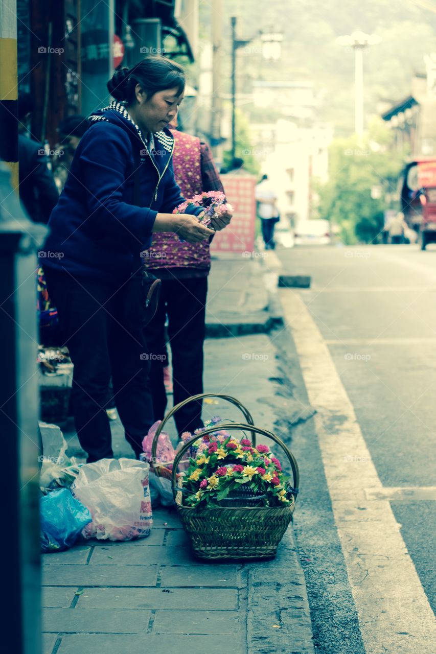 Fenghuang district, Hunan province, China - May 8, 2016 : Woman selling flowers and bouquets in a commercial street.