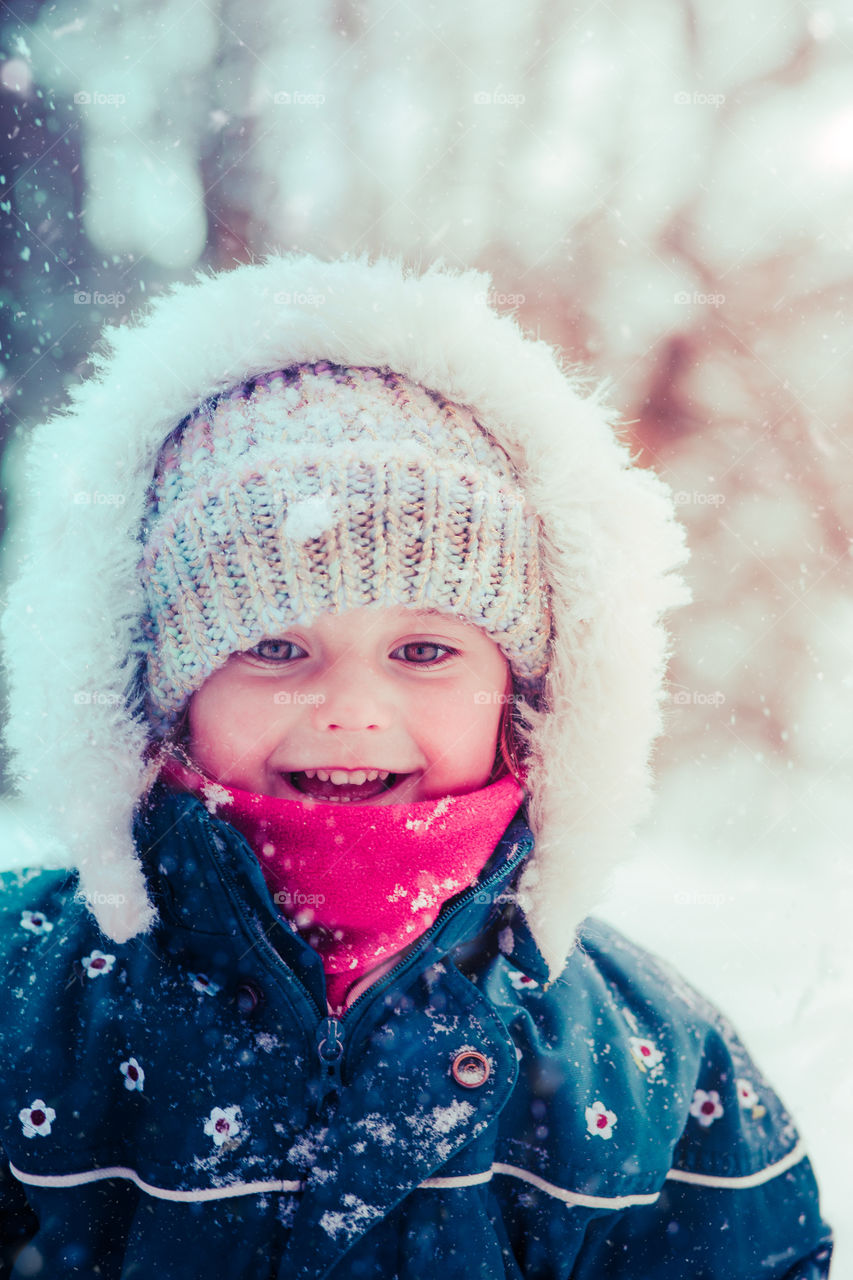 Happy smiling little girl enjoying snow. Toddler is playing outdoors in wintertime while snow falling. Toddler is wearing dark blue snowsuit and wool cap