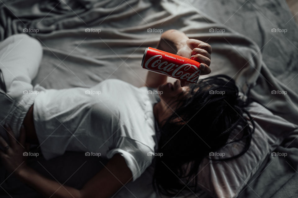 the girl lies on the bed and holds a Coca Cola