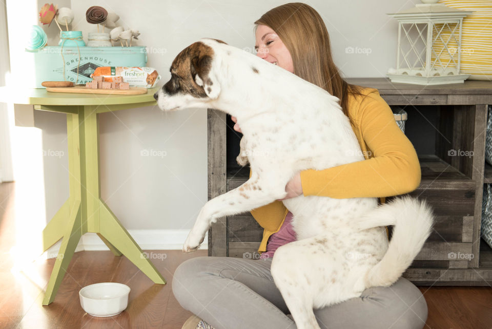 Young woman hugging her large dog while sitting on the floor indoors