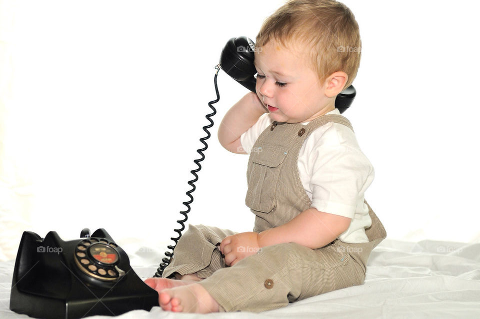 A YOUNG WHITE TODDLER BOY PRETENDS TO TALK ON AN OLD-FASHIONED