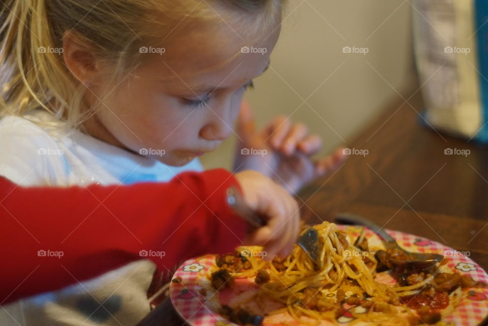 Little girl with a messy face eating spaghetti 