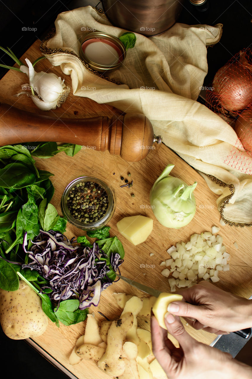 Peeling and slicing fresh market vegetables elevated view of woman’s hands working to prepare food with spinach, onions, chopped cabbage, kohlrabi, peppercorns, pepper mill, and garlic food background photography 