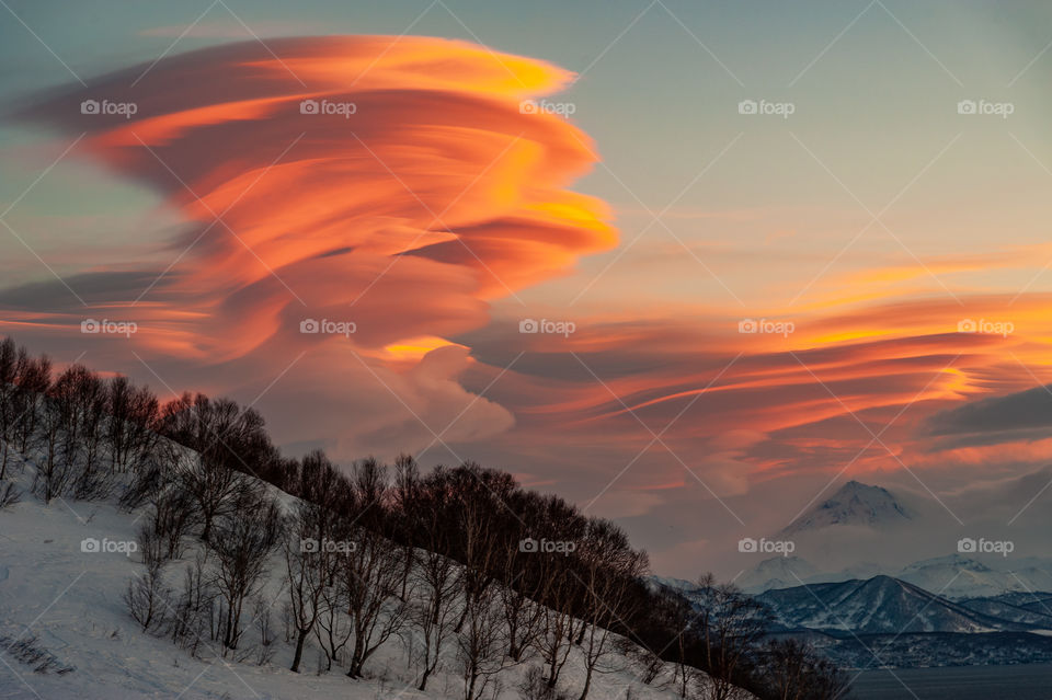 The most beautiful sunset in Kamchatka with lenticular clouds of bright scarlet color, Avachinsky volcano is visible in the background