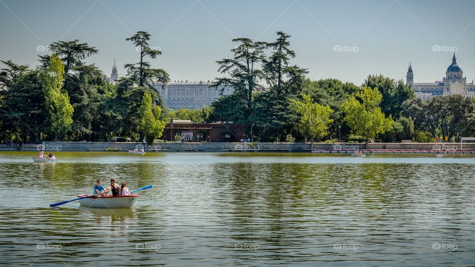 Family rowing on a pond in Madrid with Royal Palace and Almudena’s Cathedral on the background 