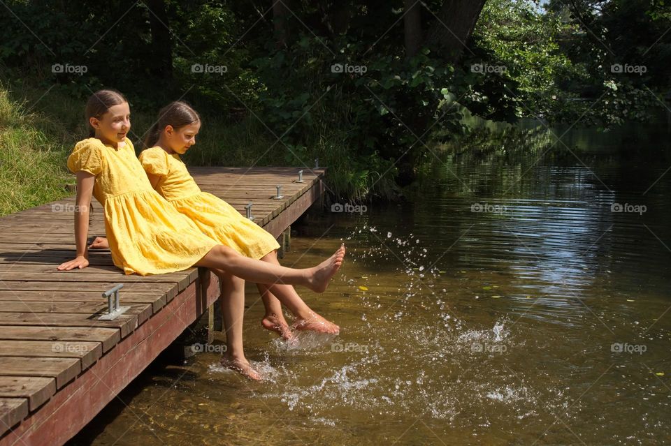 Two girls on a wooden pier by the river