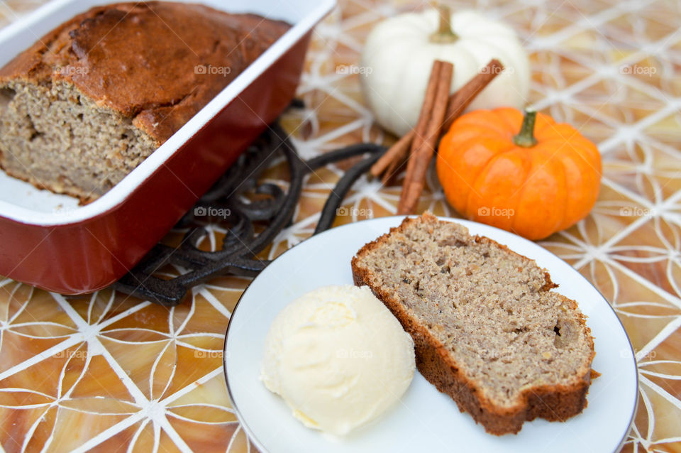 Loaf of pumpkin banana bread next to two small pumpkins and a plate with a slice of bread and scoop of ice cream