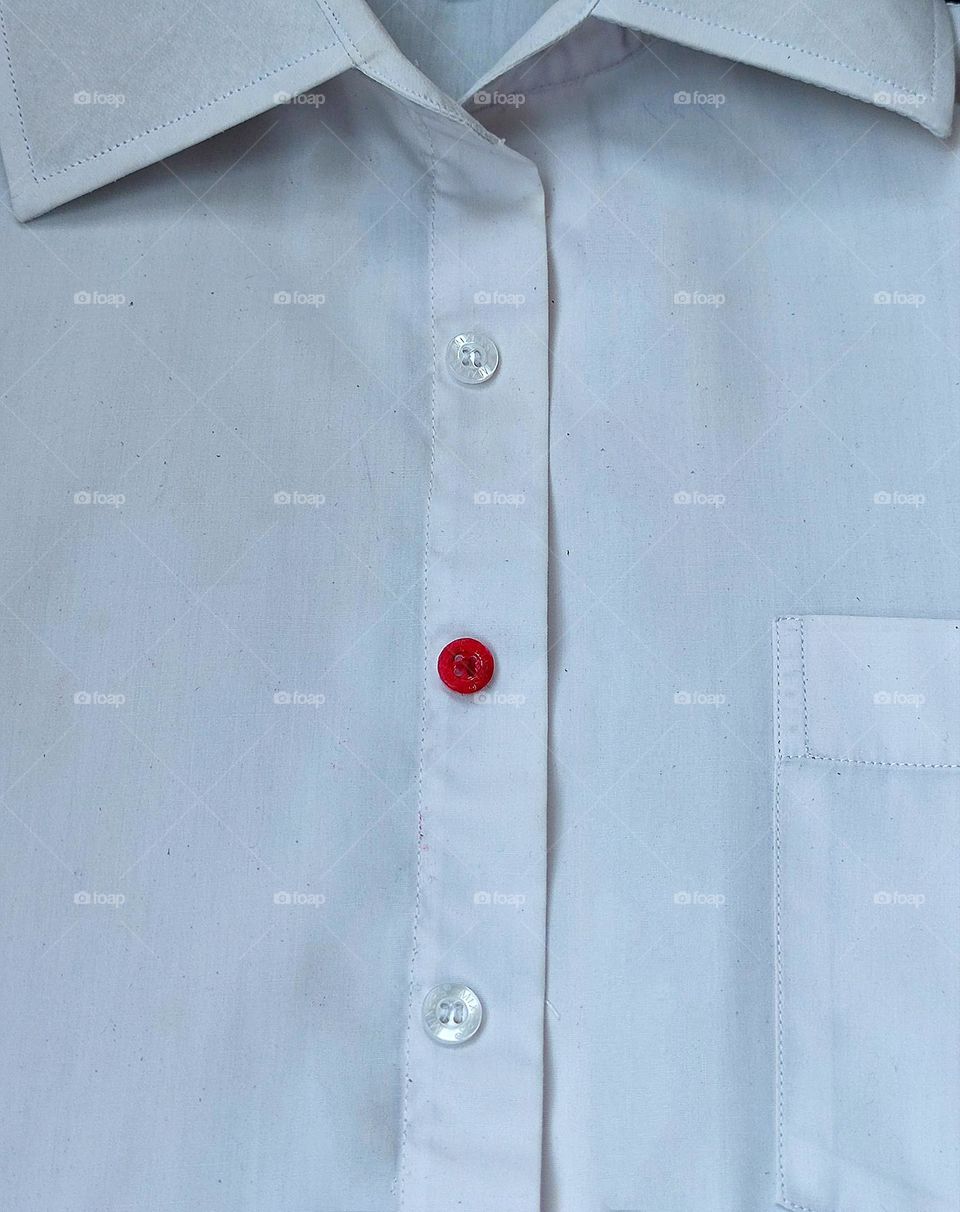 Minimalism of the object. White shirt. The shirt has a row of transparent buttons, including a bright red button. Minimalism in contrast