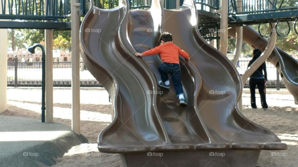 Boy on playground running up a slide.