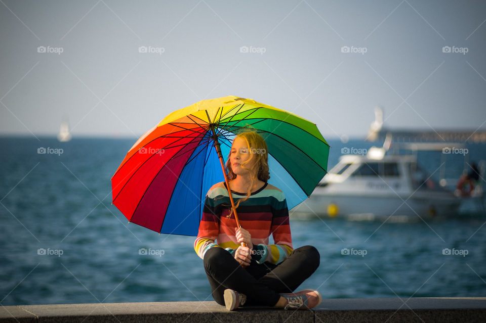 Warm autumn day, a young pretty girl in with a bright, colorful umbrella, sits on the seashore