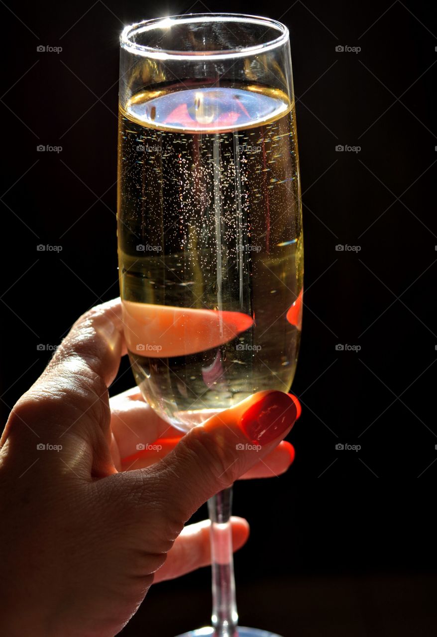 glass of champagne in the female hand in the sunlight dark background in contrast