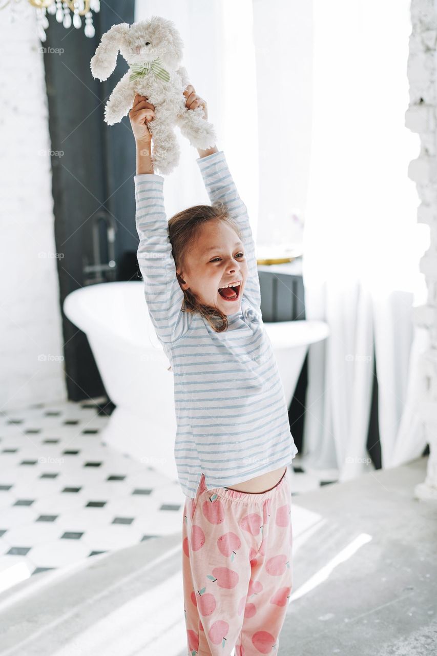 Cute little girl having fun with toy at bright bath room at home