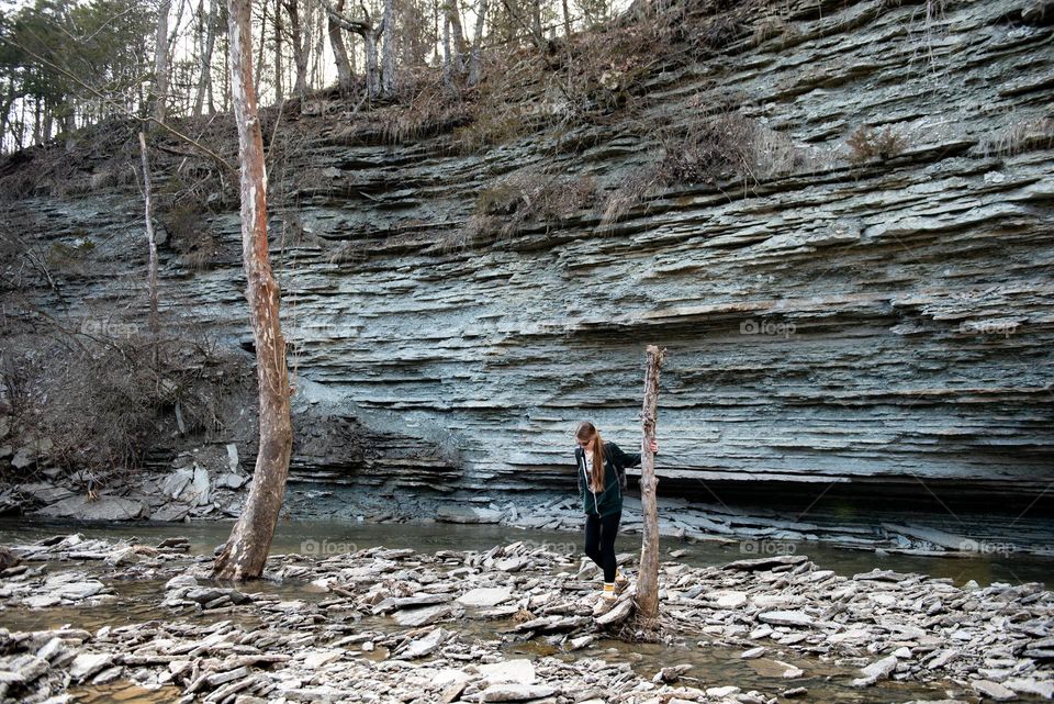 Millennial woman hiking in a rocky creek along a tall stone wall at Caesar Creek state park 