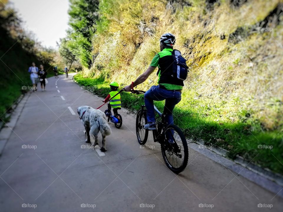 Father and son riding their bikes accompanied by their dog on a beautiful hiking trail, during a spring morning.