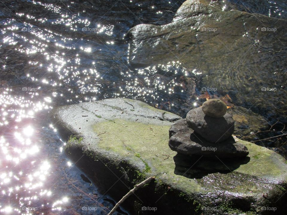 Rocks stacked in a river with the sunlight reflecting off of the water