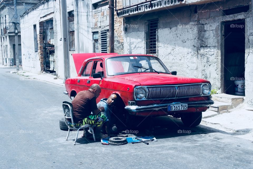 Two Men fixing an red old car in the streets of Havanna Cuba 