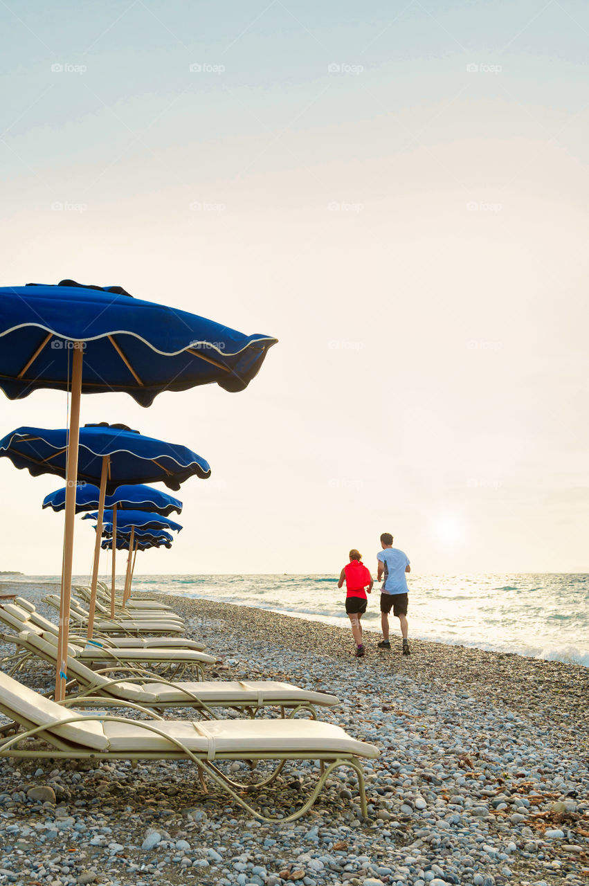 Young couple jogging along on the pebble beach during the sunset.