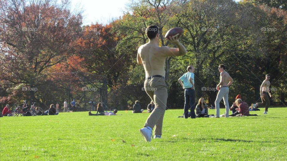 Man Throwing a Football in a City Park with his Friends on a Nice Sunny Autumn Day