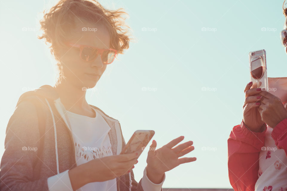 Young girl and her mother taking a photos over sea during summer vacation using smartphone camera enjoying sunny summertime day