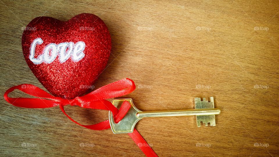 a red shiny heart with the word "love" written on it in white letters, a red ribbon attached at the bottom, and a bronze key attached to it, copy space for text