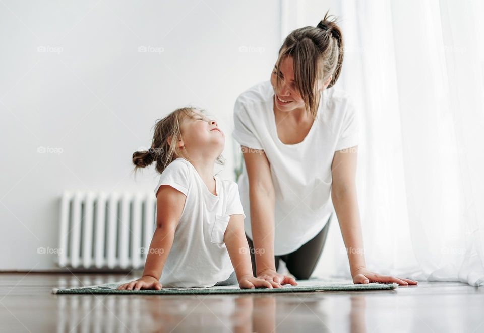 Happy mom and little daughter doing morning yoga together at bright interior home