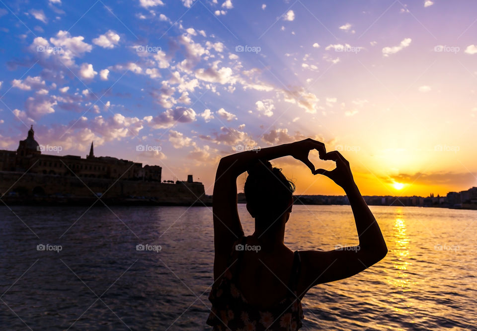 Silhouette woman making heart shaped hands at sunset 