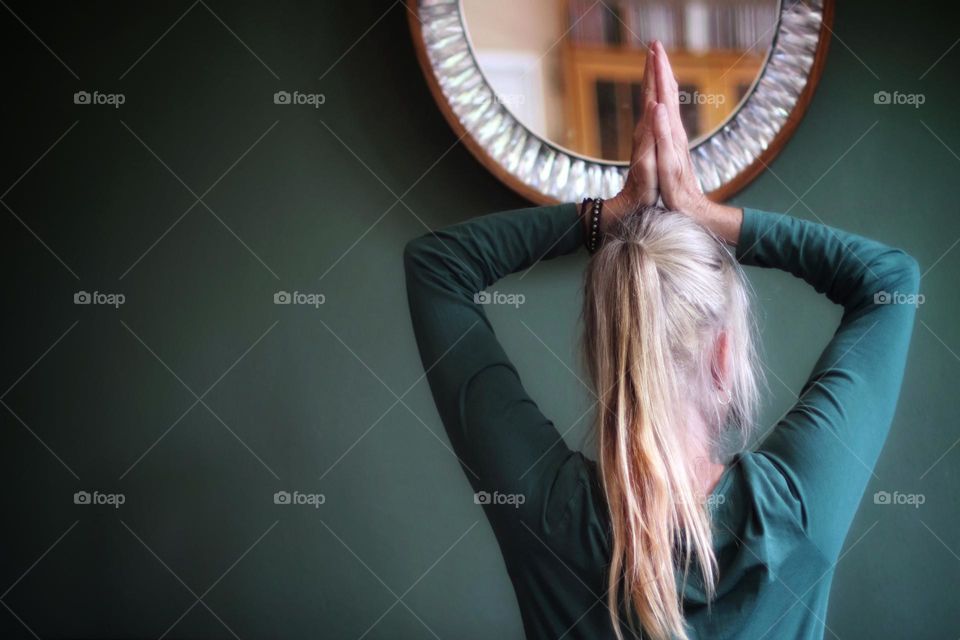 Rear view of a woman with a blonde ponytail who has her hands up in meditation